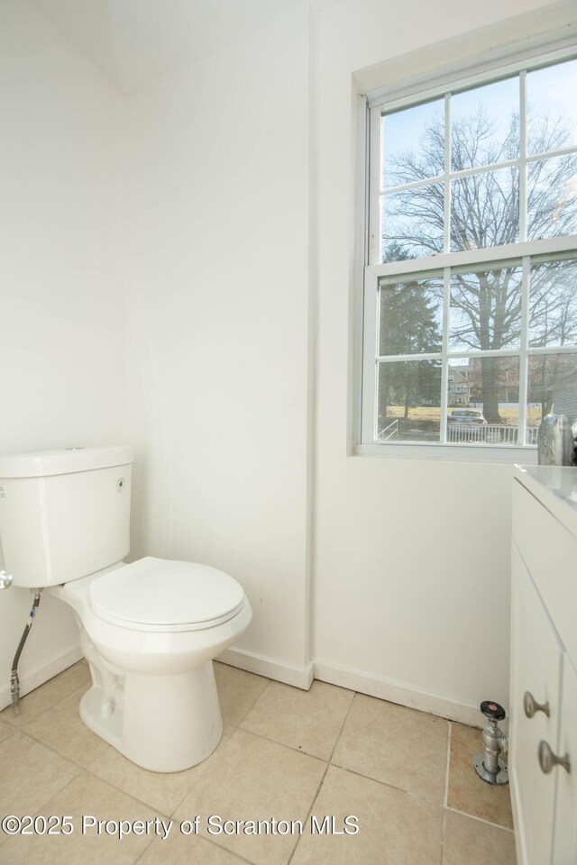 half bathroom with tile patterned flooring, baseboards, a healthy amount of sunlight, and toilet