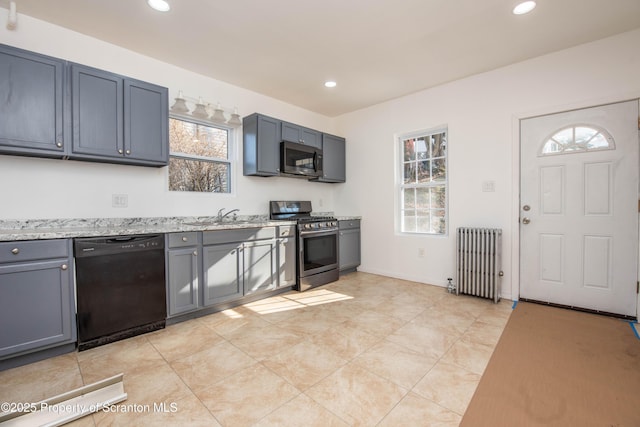 kitchen with radiator, light stone countertops, stainless steel appliances, a sink, and recessed lighting