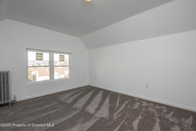 additional living space with vaulted ceiling, radiator heating unit, dark carpet, and baseboards