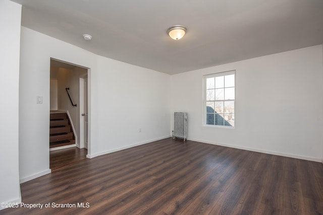 spare room featuring dark wood-type flooring, radiator, stairway, and baseboards