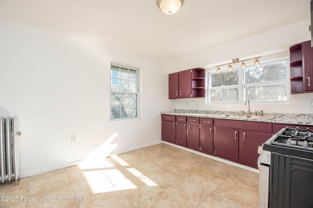 kitchen featuring baseboards, radiator heating unit, gas range oven, open shelves, and a sink