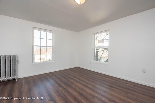 spare room featuring dark wood-style floors, radiator, and baseboards