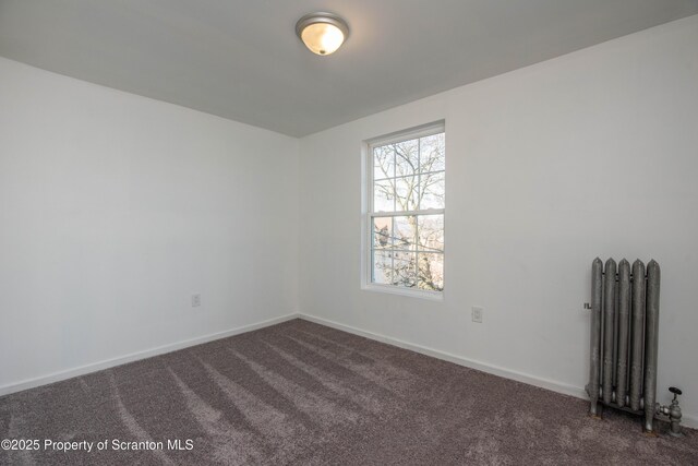 unfurnished room with baseboards, dark colored carpet, and radiator