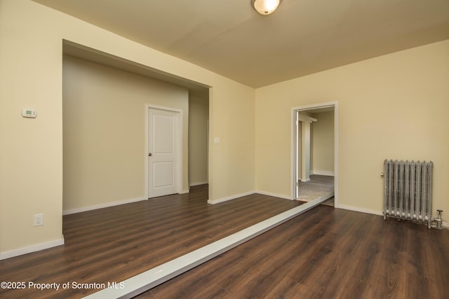 spare room featuring baseboards, dark wood finished floors, and radiator heating unit