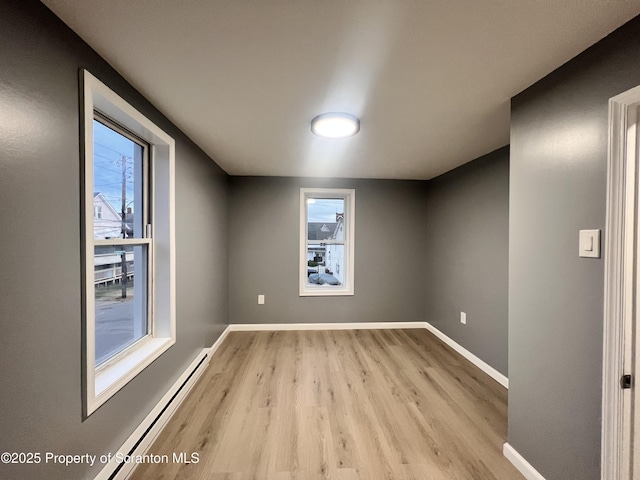 unfurnished room featuring light wood-type flooring, baseboard heating, and a healthy amount of sunlight