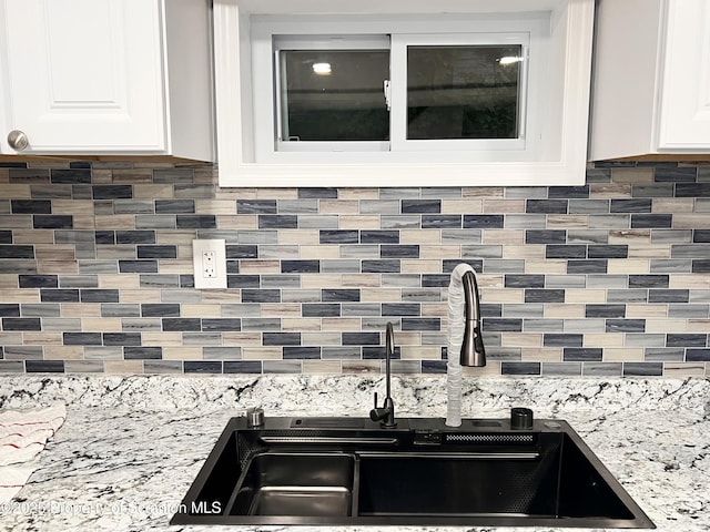 details featuring white cabinetry, decorative backsplash, sink, and light stone counters