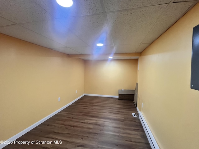 basement featuring dark hardwood / wood-style flooring, baseboard heating, and a paneled ceiling