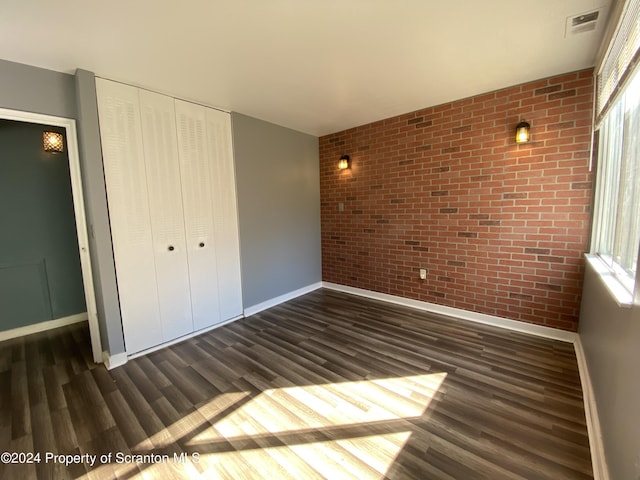 unfurnished bedroom with dark hardwood / wood-style flooring, a closet, and brick wall