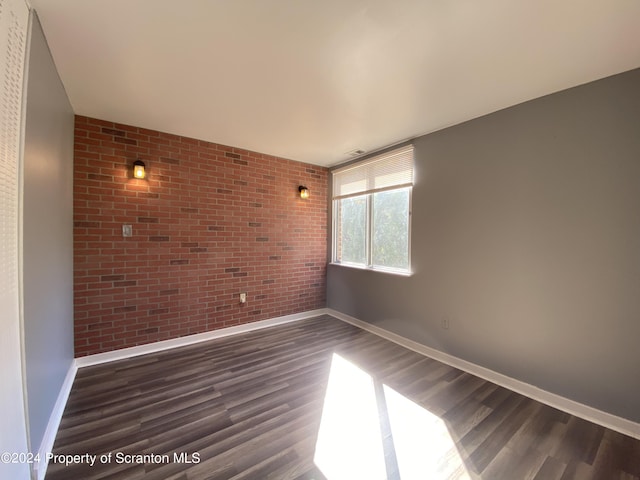 unfurnished room featuring dark wood-type flooring and brick wall