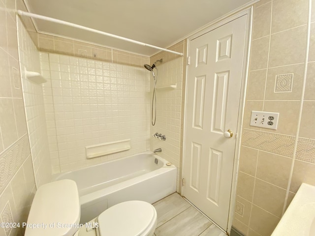 bathroom with toilet, tiled shower / bath combo, and tile walls