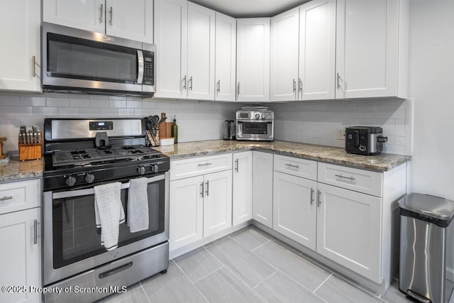 kitchen featuring stainless steel appliances, backsplash, white cabinetry, and light stone countertops