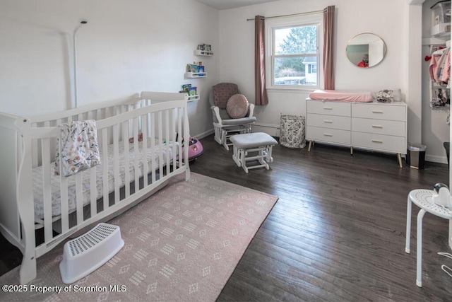 bedroom with a nursery area, baseboards, and wood finished floors