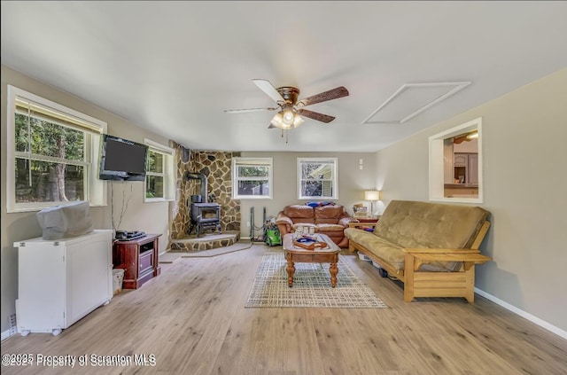 living room featuring plenty of natural light, a wood stove, ceiling fan, and light hardwood / wood-style flooring