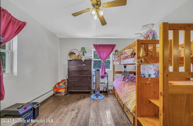 bedroom with multiple windows, hardwood / wood-style floors, a baseboard radiator, and ceiling fan