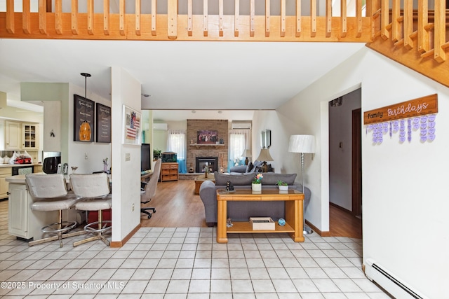 living room featuring baseboards, a fireplace, baseboard heating, a wall unit AC, and light tile patterned floors