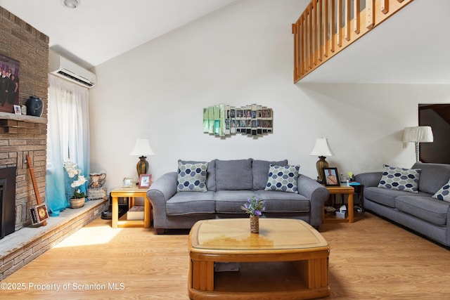 living area with lofted ceiling, wood finished floors, an AC wall unit, and a brick fireplace