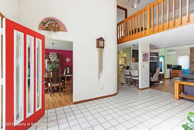 tiled foyer entrance featuring baseboards, a wall mounted air conditioner, a towering ceiling, and a chandelier