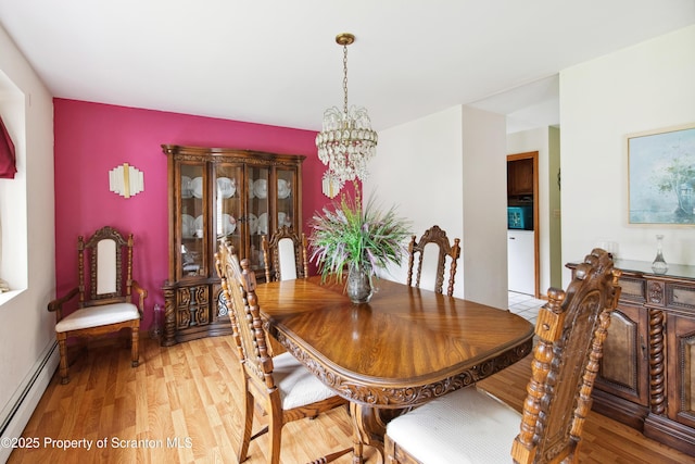 dining area with an inviting chandelier, a baseboard heating unit, and light wood-type flooring