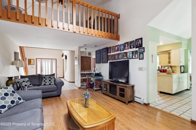 living room featuring a high ceiling, baseboards, light wood-style flooring, and a baseboard radiator