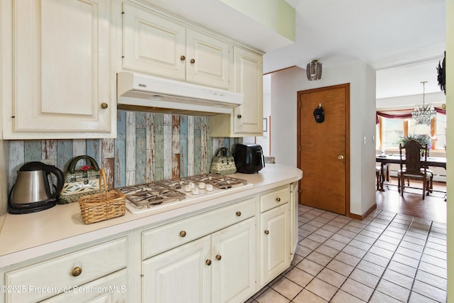 kitchen featuring light countertops, tasteful backsplash, under cabinet range hood, and light tile patterned floors