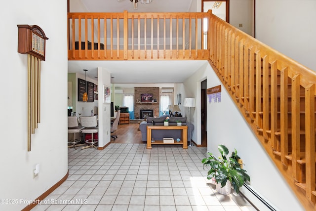 interior space featuring tile patterned floors, baseboard heating, a high ceiling, and a brick fireplace