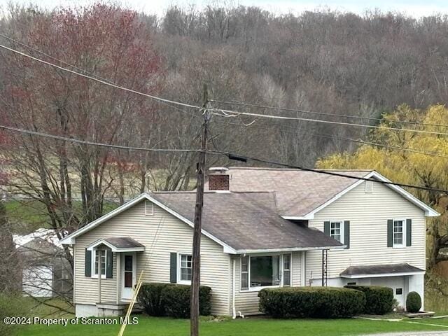 split level home with a wooded view, a chimney, and a front lawn