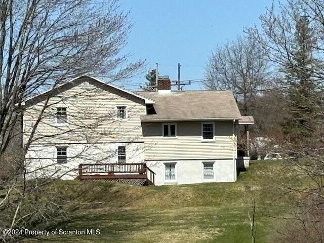 rear view of property featuring a lawn, a chimney, and a wooden deck