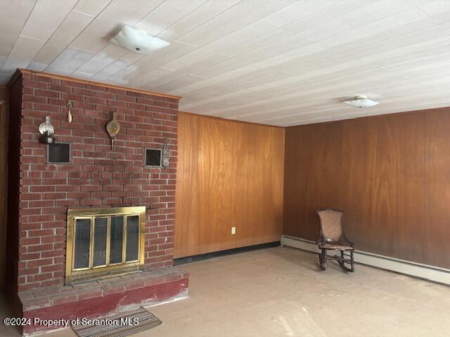 unfurnished room with a baseboard heating unit, a brick fireplace, and wooden walls