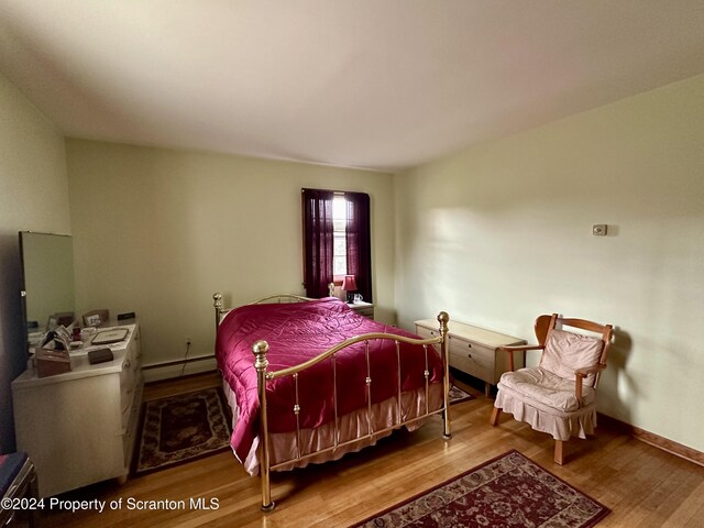 bedroom with a baseboard radiator, wood finished floors, and baseboards