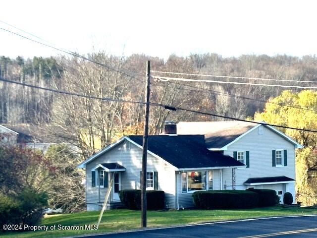 view of front of home featuring a wooded view, a chimney, and a front lawn