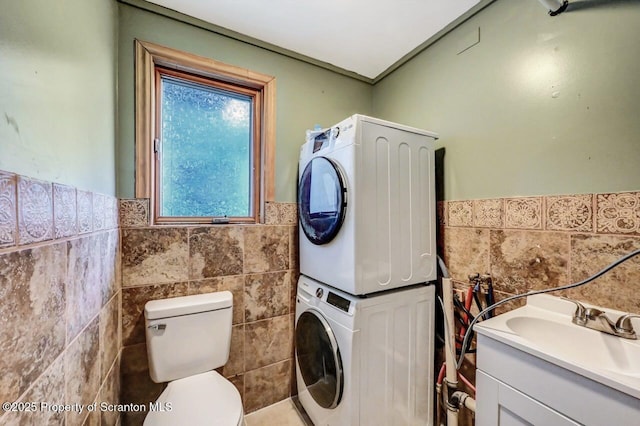 clothes washing area featuring tile walls, stacked washer and dryer, and sink