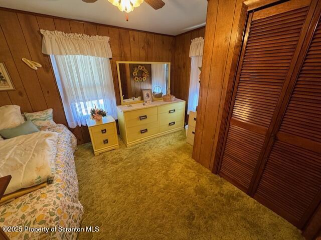 carpeted bedroom with wood walls, ceiling fan, and a closet