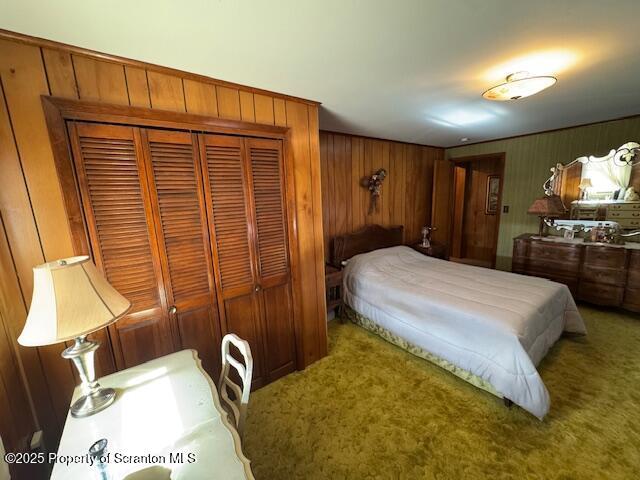 carpeted bedroom featuring wood walls and a closet