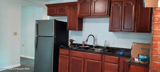 kitchen featuring dark stone countertops, black refrigerator, and sink