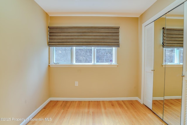 unfurnished bedroom featuring multiple windows, wood finished floors, a closet, and baseboards