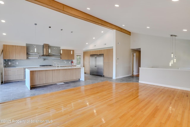 kitchen featuring beam ceiling, stainless steel built in fridge, light countertops, wall chimney range hood, and modern cabinets