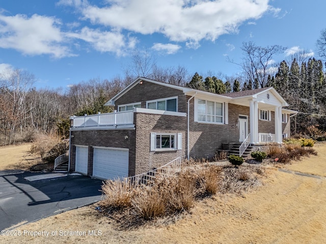 bi-level home with aphalt driveway, a balcony, and brick siding