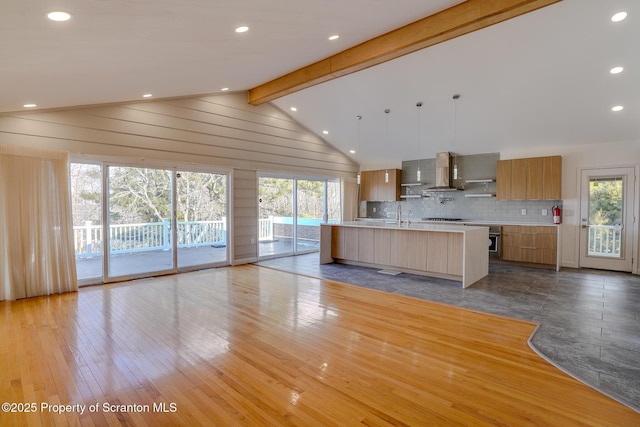 kitchen with modern cabinets, backsplash, wall chimney exhaust hood, light countertops, and vaulted ceiling with beams