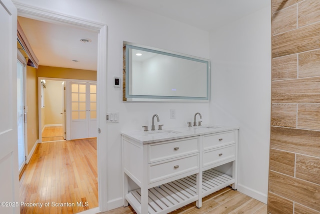 bathroom featuring a sink, baseboards, wood finished floors, and double vanity