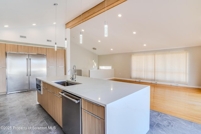 kitchen featuring lofted ceiling with beams, a kitchen island with sink, a sink, built in appliances, and modern cabinets