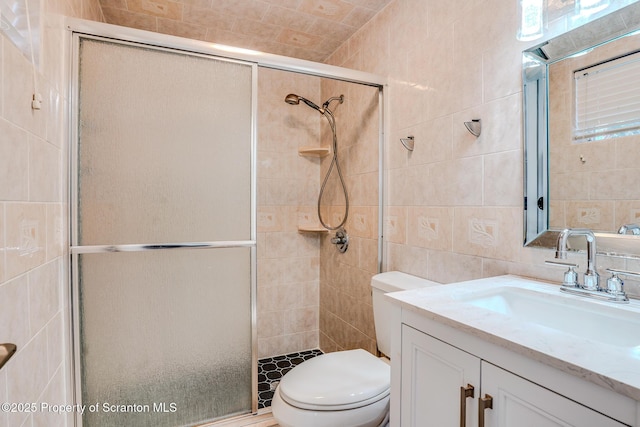 bathroom with toilet, tile walls, a stall shower, and vanity