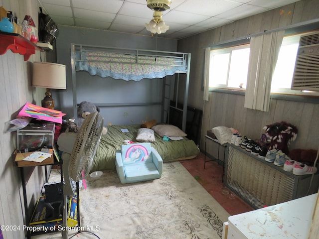 bedroom featuring an AC wall unit, wood walls, and a drop ceiling