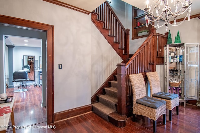 staircase featuring hardwood / wood-style flooring, ornamental molding, and an inviting chandelier