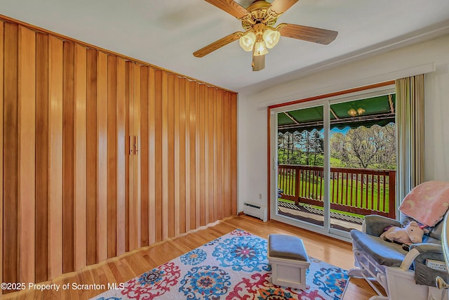 living area with a baseboard radiator, ceiling fan, wood finished floors, and wood walls
