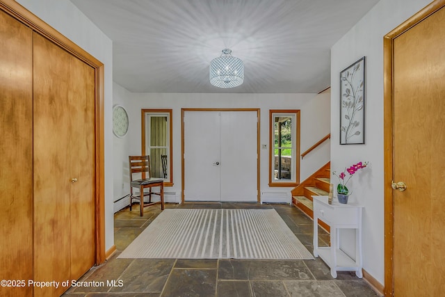 entrance foyer featuring an inviting chandelier, stone tile floors, stairs, and a baseboard heating unit