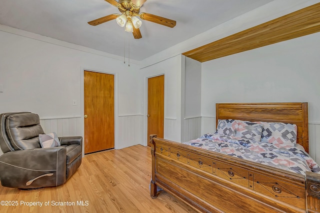bedroom with a ceiling fan, wainscoting, and light wood-style flooring