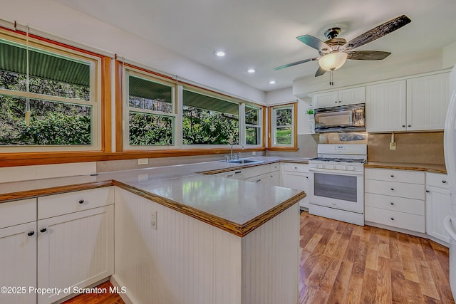 kitchen featuring white cabinets, a peninsula, black microwave, and white range with gas stovetop