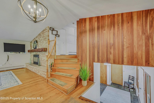 staircase with baseboard heating, wood walls, wood finished floors, a notable chandelier, and lofted ceiling