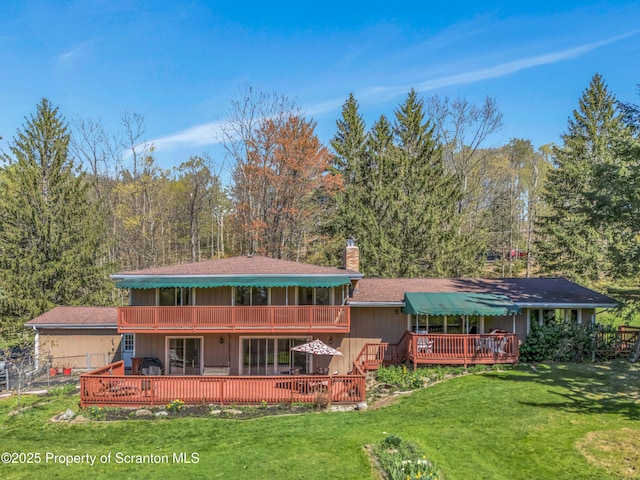 rear view of house featuring a chimney, a lawn, a wooded view, and a deck