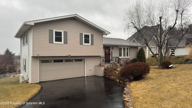 tri-level home with a garage, a front yard, aphalt driveway, and brick siding